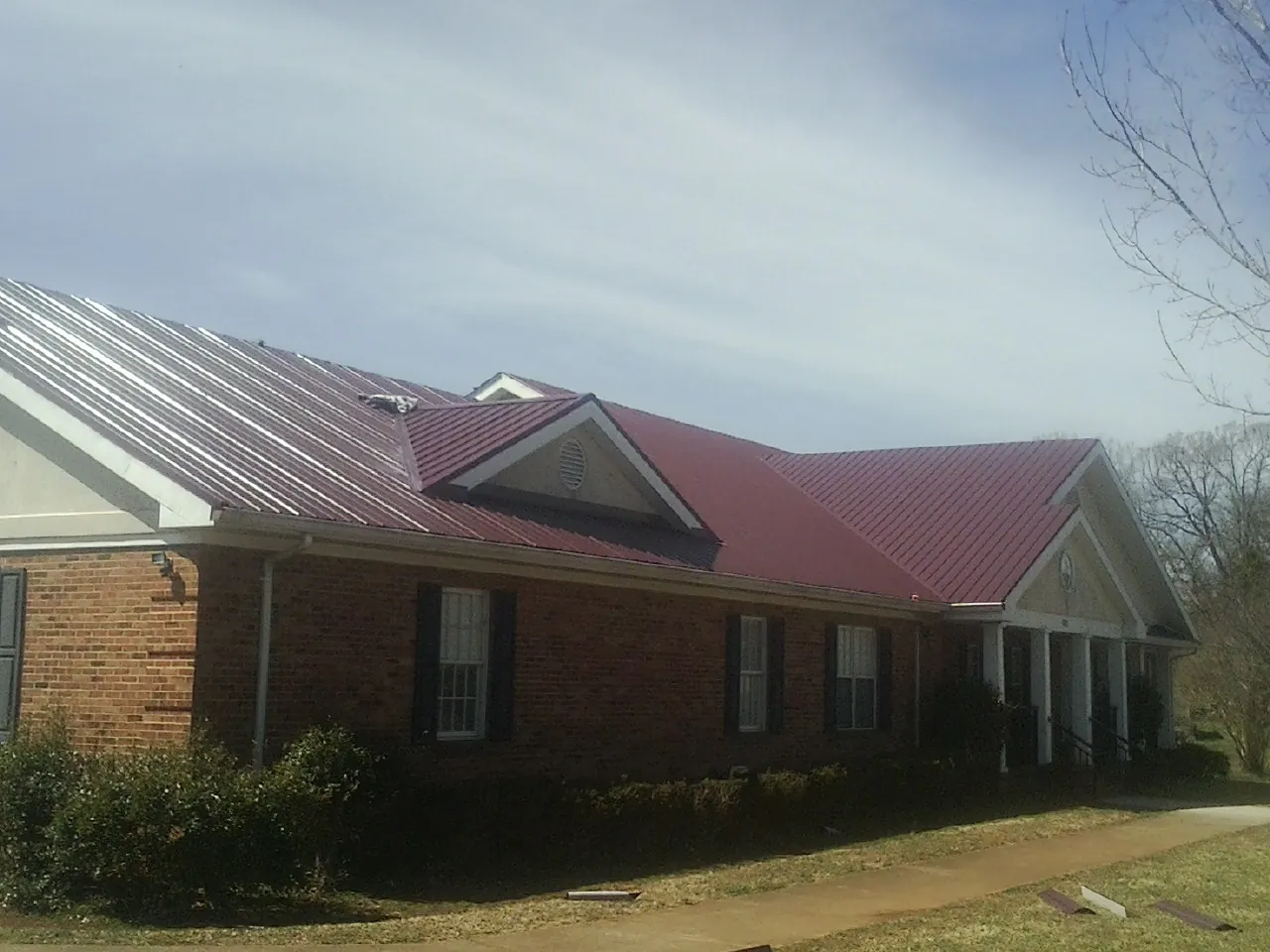 Red metal roof with gabled entries on a long brick building, from a Hail Damage Roof Repair job in Hagerstown