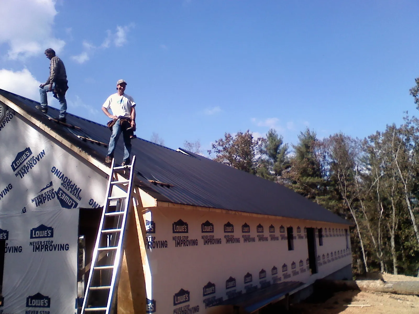 Two roofers standing on a long dark metal roof over a wrapped building in Hagerstown