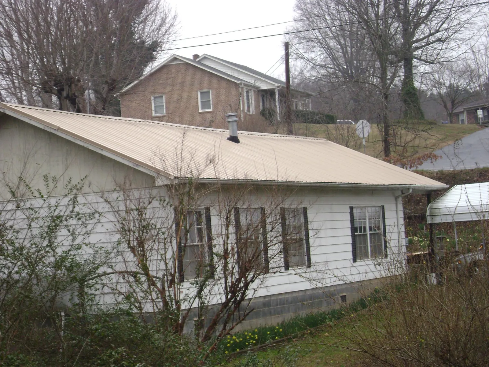 Tan metal roof on a white sided house set into a hillside — Commercial Roofing by Roofing Brothers in Hagerstown